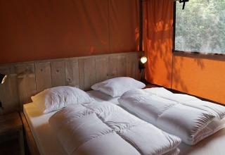 Slaapruimte in Glampingtent Desert met tweepersoonsbed, houten hoofdbord en oranje tentdoek.