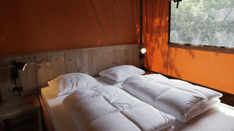 Área de descanso en Glampingtent Desert con cama doble, detalles en madera y paredes naranjas.
