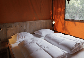 Área de descanso en Glampingtent Desert con cama doble, detalles en madera y paredes naranjas.