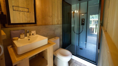 Baño moderno en Glampingtent Desert con lavabo, inodoro y ducha de vidrio, rodeado de decoración de madera.