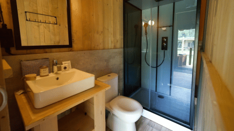 Salle de bain moderne de Glampingtent Desert avec lavabo, toilettes et douche vitrée dans un décor bois.