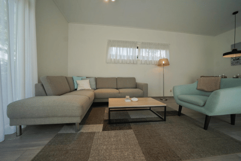 Modernes Wohnzimmer mit grauem Ecksofa, blauem Sessel und Couchtisch im Pavilion bei EuroParcs Veluwemeer, Niederlande.