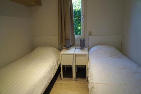 Zwei Einzelbetten mit weißen Bezügen und Nachttischen im Zimmer des Pavilion bei EuroParcs Veluwemeer, Niederlande.