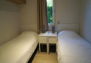 Dos camas individuales con ropa de cama blanca y mesitas en una habitación del Pavilion en EuroParcs Veluwemeer, Países Bajos.