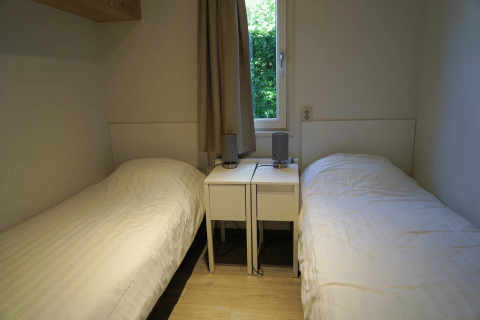 Zwei Einzelbetten mit weißen Bezügen und Nachttischen im Zimmer des Pavilion bei EuroParcs Veluwemeer, Niederlande.