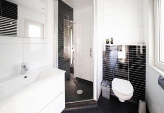 Bagno moderno in un lodge con WC sospeso, doccia chiusa, lavabo bianco e piastrelle nere sul muro.