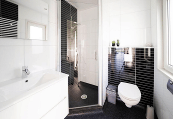 Baño moderno en una cabaña con inodoro suspendido, ducha acristalada, lavabo blanco y azulejos negros.