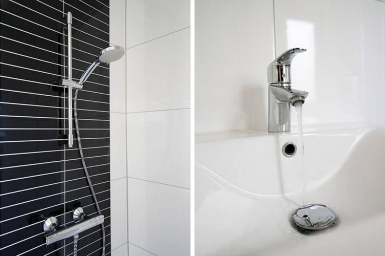 Ducha moderna con pared de azulejos blancos y negros y grifo brillante junto a lavabo en una cabaña.