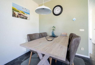 Comedor moderno en un lodge con mesa de madera, sillas acolchadas y decoración de pared con reloj.
