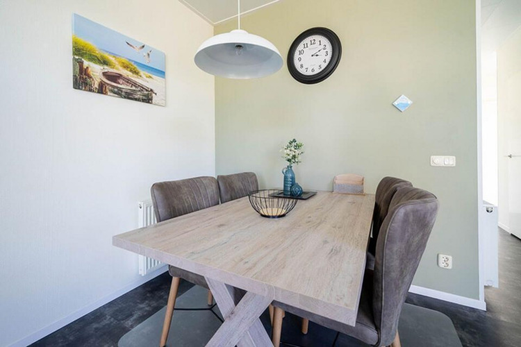Comedor moderno en un lodge con mesa de madera, sillas acolchadas y decoración de pared con reloj.
