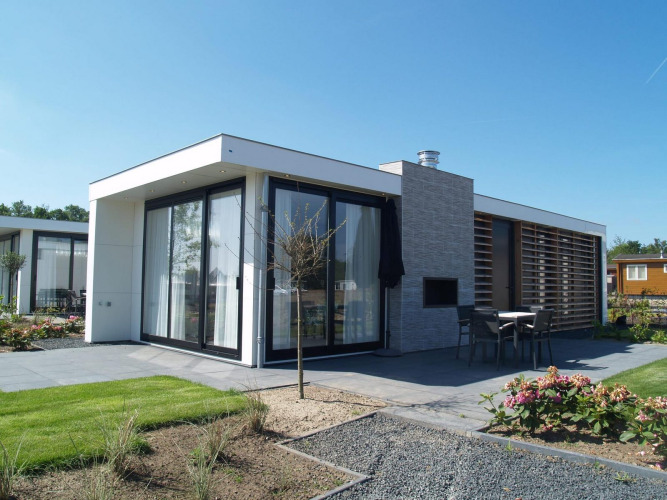 Lodge tipo pabellón moderno con grandes ventanales, terraza y jardín bajo un cielo azul, ideal para relajarse.