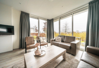 Salon lumineux et moderne d’un pavillon à EuroParcs Veluwemeer, Pays-Bas, avec de grandes fenêtres et un décor cosy.