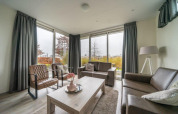 Sala moderna con ventanales, cortinas grises y sofás de cuero en el lodge Pavilion de EuroParcs Veluwemeer.
