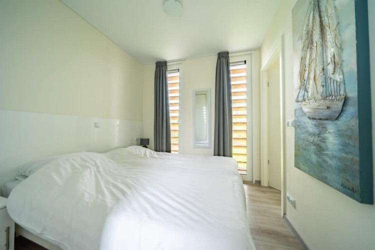 Dormitorio luminoso con dos camas individuales, pintura y ventanas altas en Pavilion de EuroParcs Veluwemeer, Países Bajos.