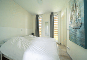 Chambre lumineuse avec deux lits simples, tableau et grandes fenêtres au Pavilion d’EuroParcs Veluwemeer, Pays-Bas.