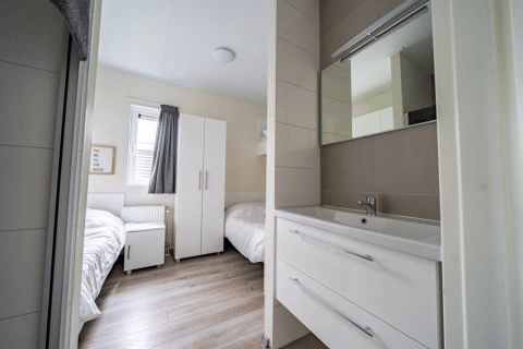 Modernes Lodge-Zimmer im Pavilion bei EuroParcs Veluwemeer, Niederlande, mit zwei Betten und Waschbecken.