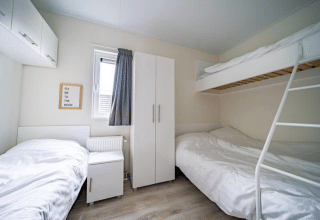 Helles Zimmer mit Etagenbett, Einzelbett, Schrank und Wandschild im Pavilion bei EuroParcs Veluwemeer, Niederlande.