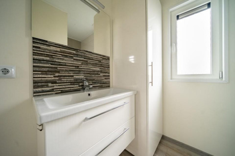 Lavabo de salle de bain moderne avec miroir, carrelage décoratif, armoire et fenêtre au Pavilion d’EuroParcs Veluwemeer.