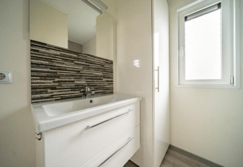 Lavabo de salle de bain moderne avec miroir, carrelage décoratif, armoire et fenêtre au Pavilion d’EuroParcs Veluwemeer.