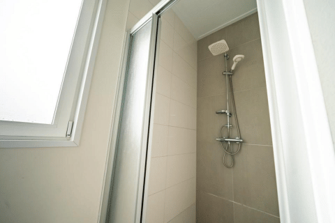 Ducha moderna con puerta de vidrio y ventana en el Pavilion de EuroParcs Veluwemeer, Países Bajos.