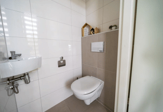 Moderne, hvidflisebeklædt badeværelse på Pavilion ved EuroParcs Veluwemeer med væghængt toilet.