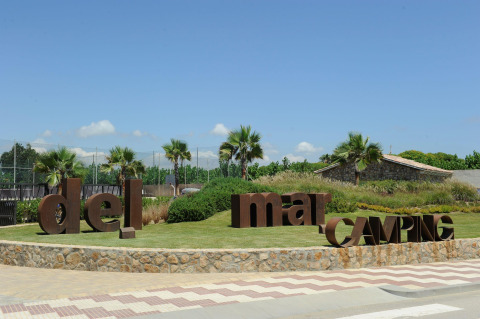Entrada del camping Camping del Mar en Cataluña, España, con palmeras y grandes letras marrones en el césped.