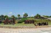 Entrance of Camping del Mar holiday park in Catalonia, Spain, with palm trees and large brown letters on grass.