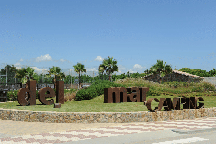 Entrée du Camping del Mar en Catalogne, Espagne, avec des palmiers et de grandes lettres sur la pelouse.