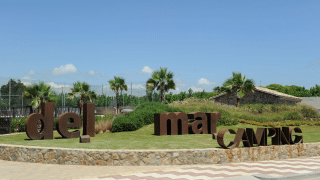 Ingang van Camping del Mar vakantiepark in Catalonië, Spanje, met palmbomen en grote bruine letters op gras.