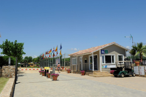 Entrada al Camping del Mar en Cataluña, España, con banderas, recepción y un carrito de golf bajo el sol.