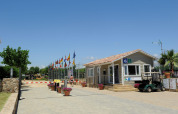 Indgang til Camping del Mar feriepark i Catalonien, Spanien, med flag, reception og golfvogn i solskin.