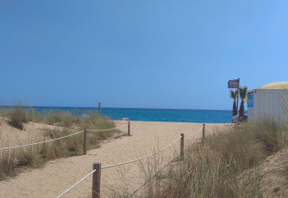 Zandweg naar het strand bij Camping del Mar in Catalonië, Spanje met zeezicht en palmbomen.