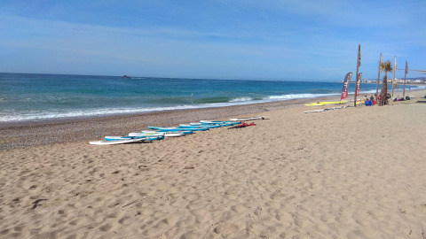 Playa en Camping del Mar, Cataluña, España, con tablas de surf sobre la arena y el mar de fondo azul.