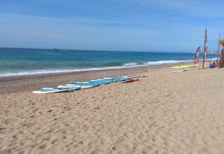 Strandzicht bij Camping del Mar in Catalonië, Spanje, met surfplanken op het zand en kalme zee op de achtergrond.