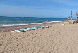 Strandbillede fra Camping del Mar i Catalonien, Spanien, med surfbrætter på sandet og roligt hav.