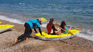 Tres personas se preparan para navegar en kayak amarillo desde la playa de piedras en Camping del Mar, Cataluña.