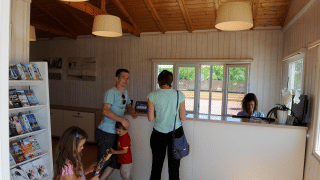 Familia en la recepción de Camping del Mar, parque vacacional en Cataluña, España, con folletos visibles.