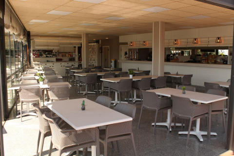 Cafetería luminosa y moderna en Camping del Mar, Cataluña, España, con varias mesas y sillas.