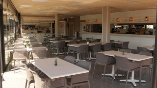 Cafetería luminosa y moderna en Camping del Mar, Cataluña, España, con varias mesas y sillas.