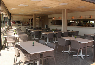 Cafetería luminosa y moderna en Camping del Mar, Cataluña, España, con varias mesas y sillas.