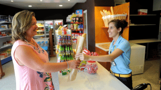 Cliente recibe una baguette de una empleada sonriente en la tienda de Camping del Mar en Cataluña, España.