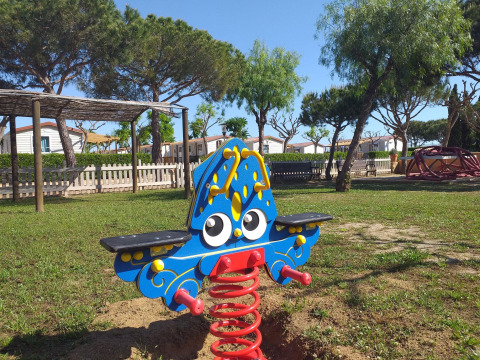 Farbiges Wipptier auf einem Spielplatz im Camping del Mar, Katalonien, Spanien, umgeben von Bäumen.