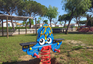 Jeu à ressort coloré sur l’aire de jeux de Camping del Mar, Catalogne, Espagne, entouré d’arbres.