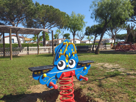 Jeu à ressort coloré sur l’aire de jeux de Camping del Mar, Catalogne, Espagne, entouré d’arbres.
