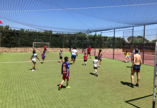 Børn og voksne spiller fodbold på en græsbanen i solen på Camping del Mar feriested i Catalonien, Spanien.