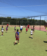 Børn og voksne spiller fodbold på en græsbanen i solen på Camping del Mar feriested i Catalonien, Spanien.
