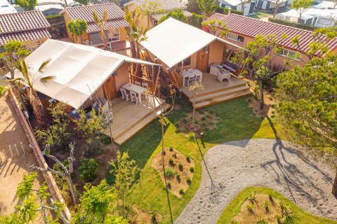 Luftfoto af Glamping Mar safari telt med træterrasse, borde, stole og grønne omgivelser i solen.