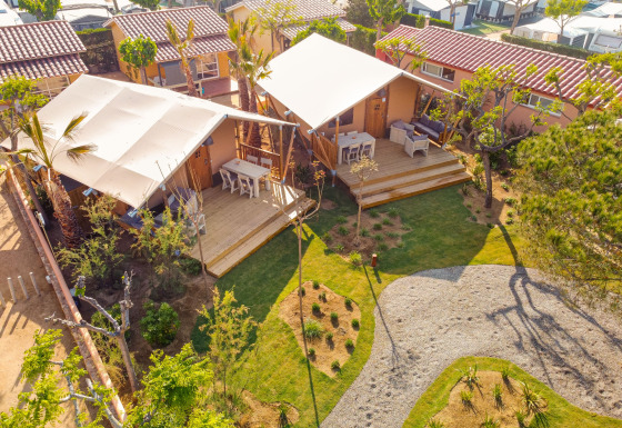 Luftfoto af Glamping Mar safari telt med træterrasse, borde, stole og grønne omgivelser i solen.