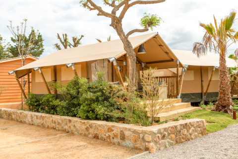 Tenda safari moderna al Glamping Mar con veranda in legno, piante verdi e un clima soleggiato e limpido.