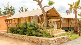 A modern safari tent at Glamping Mar with a wooden porch, lush greenery, and clear, sunny skies.